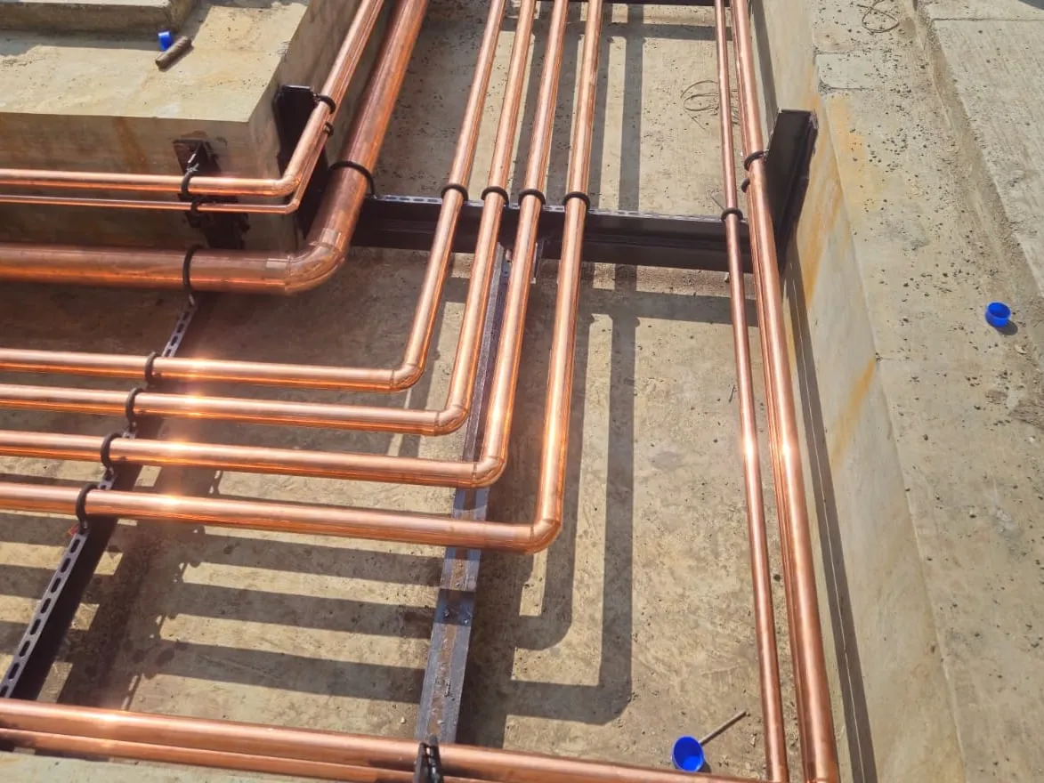 Copper pipelines on steel supports in a concrete service trench.